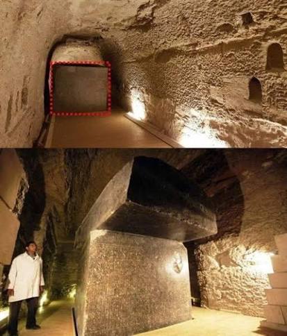A person in a white coat standing beside one of the Serapeum of Saqqara stone sarcophagi, providing scale